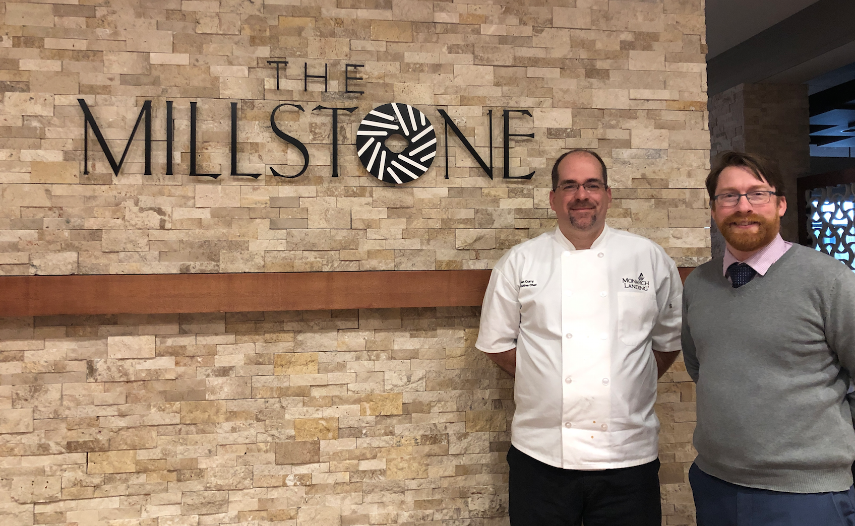 Photo of two senior living staff next to The Millstone entrance sign