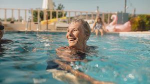 Senior woman swimming in a swimming pool while on holiday in Paphos, Cyprus. She is turning her head as she swims to laugh at her friends.