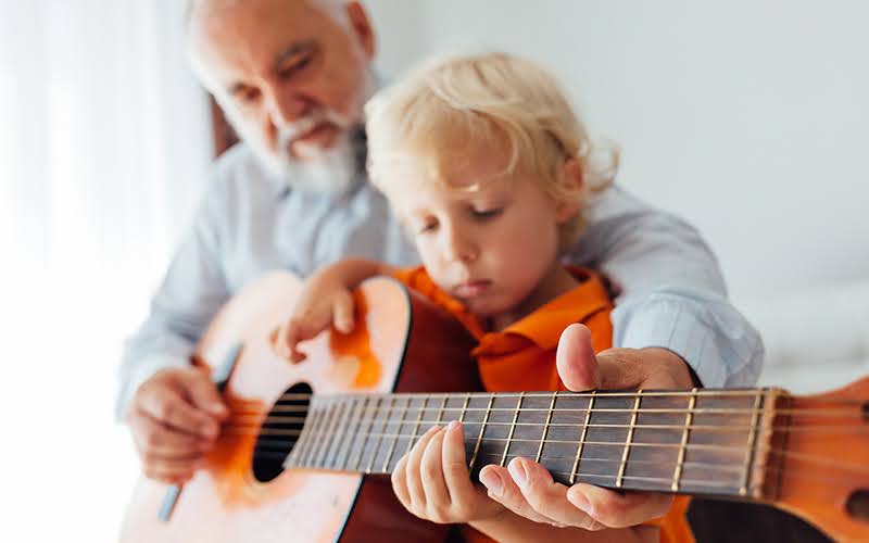 Grandpa learning his grandson to play guitar in close up.
